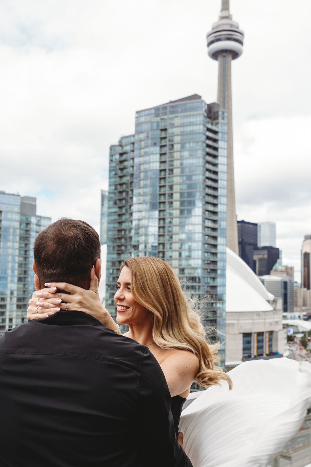 Couple sharing romantic moment on rooftop with Toronto skyline and CN Tower in background.