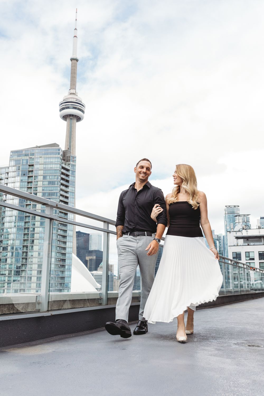 A couple poses on a rooftop terrace with Toronto's CN Tower and modern skyscrapers in the background.