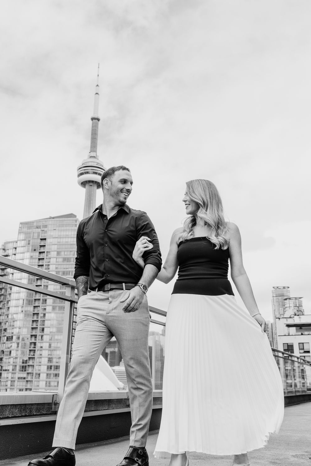 Black and white photo of a stylish couple on a Toronto rooftop with the CN Tower behind them.