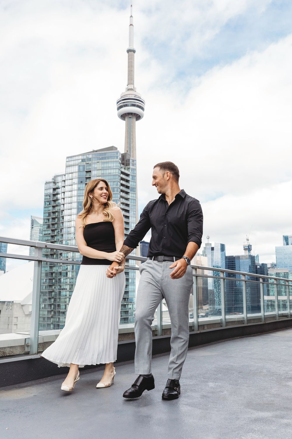 Dancing couple on urban rooftop with white dress and black shirt against Toronto cityscape backdrop.