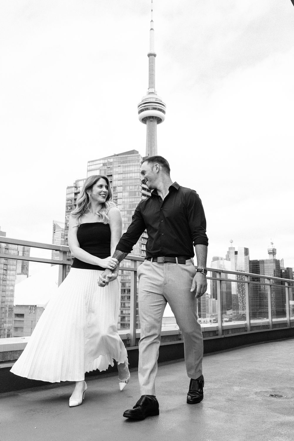 A couple shares a romantic moment on a rooftop patio with the CN Tower visible in the background.