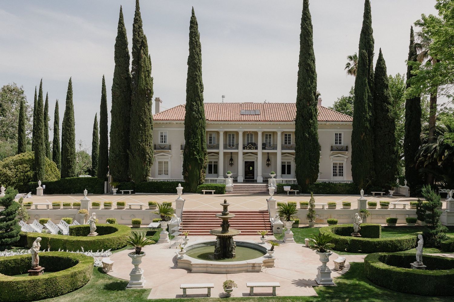 Panoramic view of a formal garden with tall cypress trees, manicured hedges, and classical statuary.