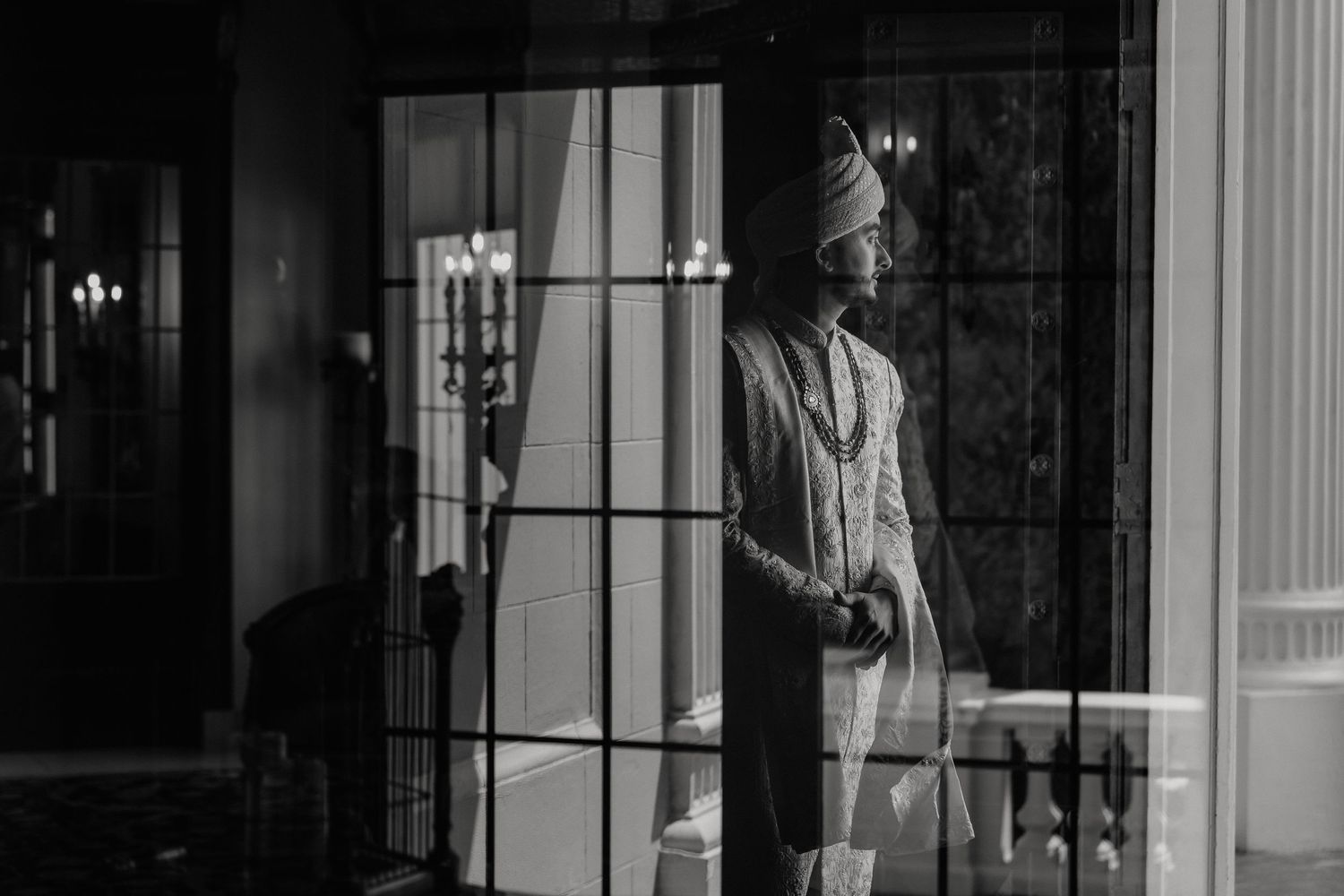 Black and white image showing a figure standing by a window in dramatic lighting.