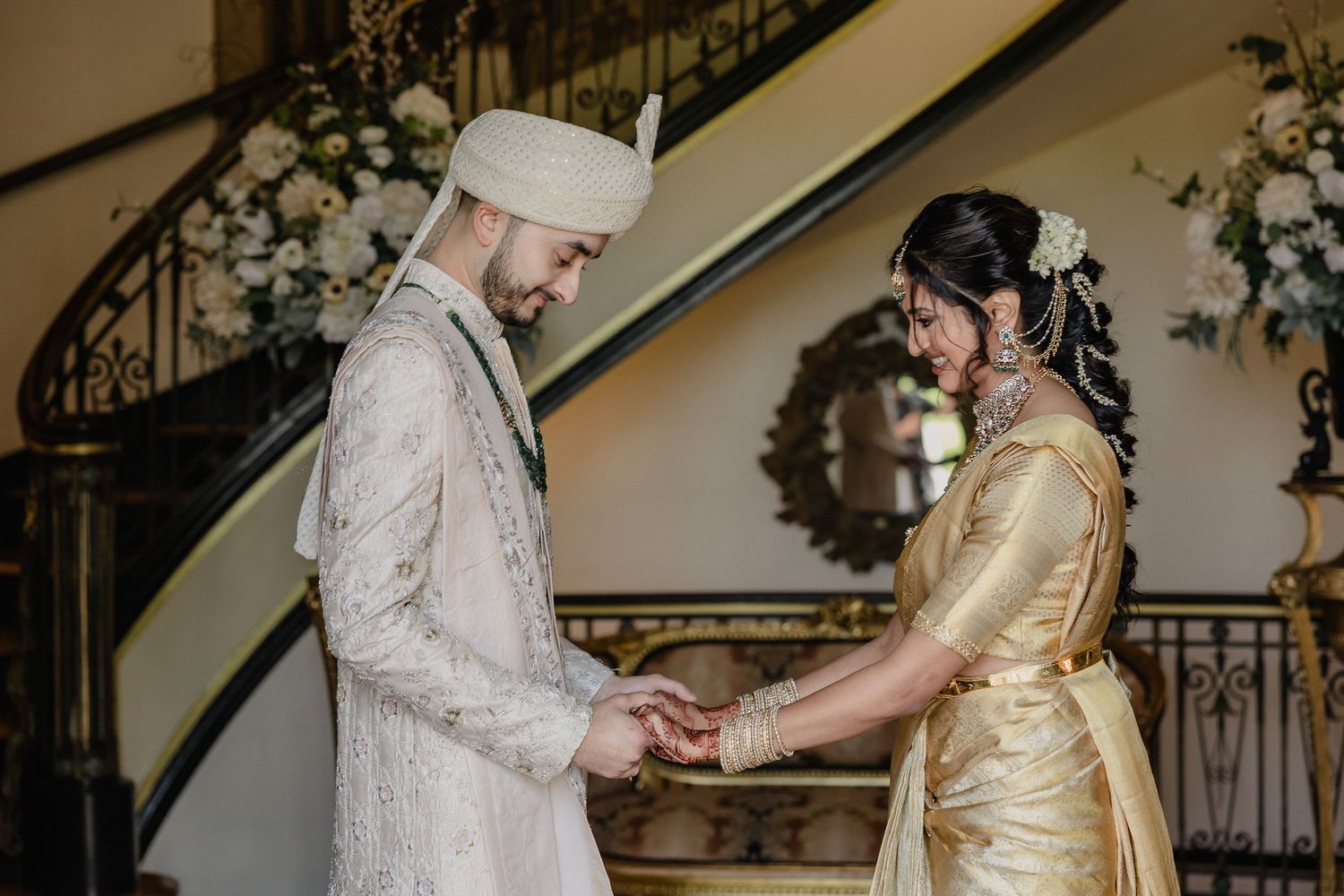 Traditional wedding ceremony with couple in cultural attire exchanging vows by an elegant staircase.