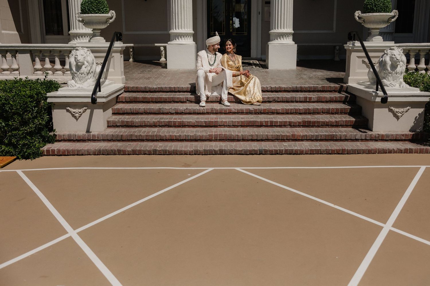 Wedding couple sitting on grand white stone steps with geometric patterns.