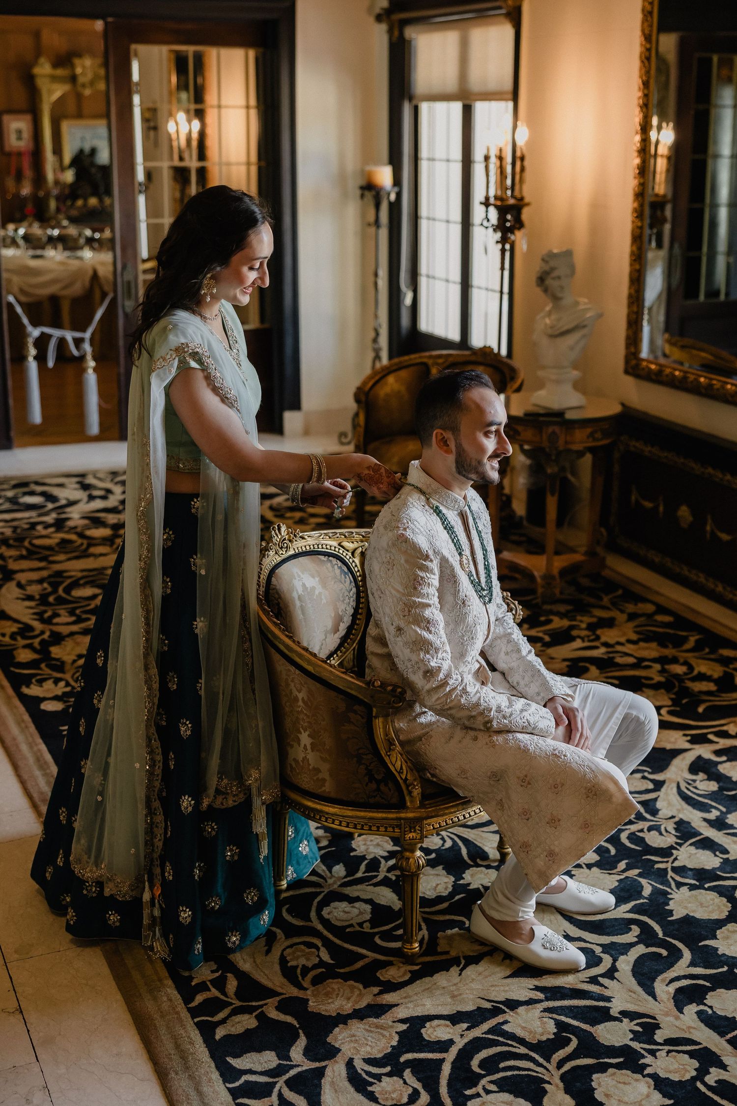 A couple in traditional South Asian wedding attire share an intimate moment in an elegantly decorated room.