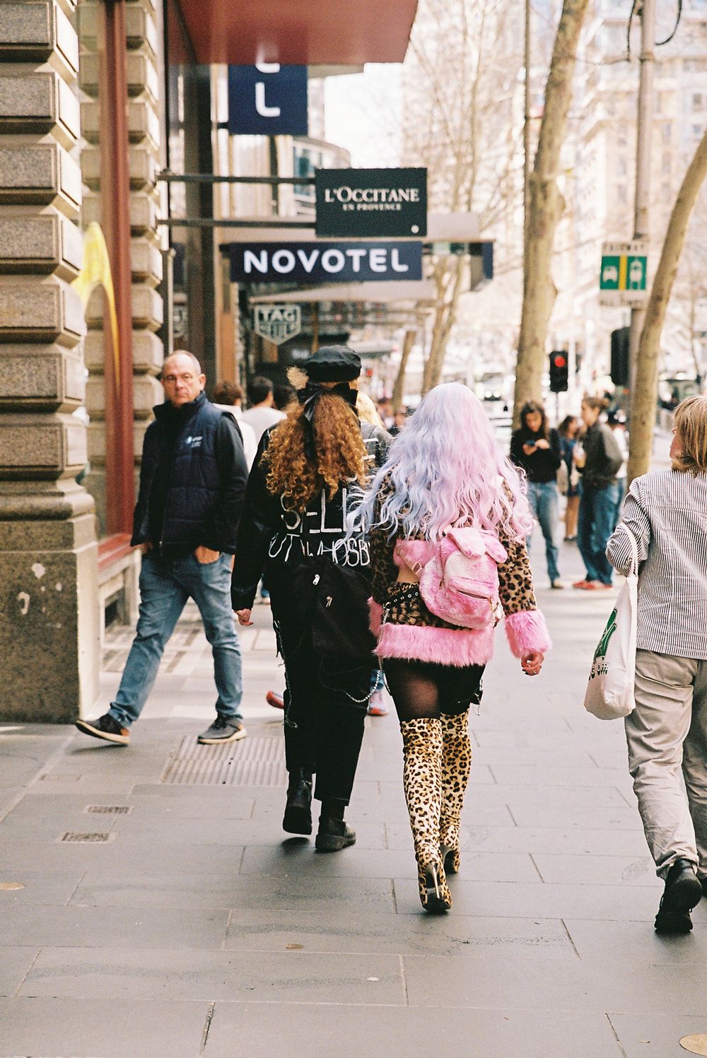 People walking on a city sidewalk wearing casual clothing and animal print patterns on a sunny day.