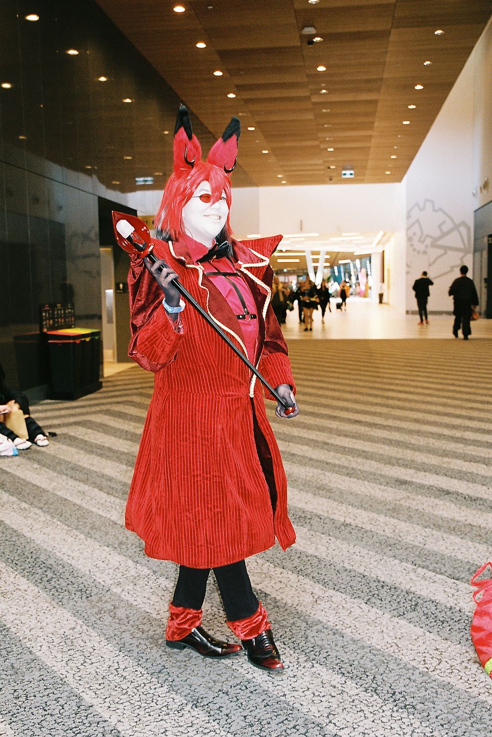 A person in a bright red corduroy outfit stands in a modern hallway with striped flooring and recessed lighting.