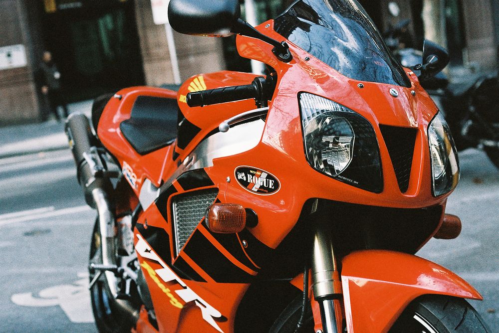 Orange Kawasaki Ninja motorcycle parked on city street with blurred urban background.