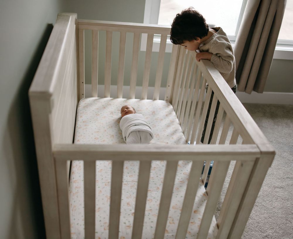 Someone assembles a white wooden crib in a bright room while following the instruction manual.