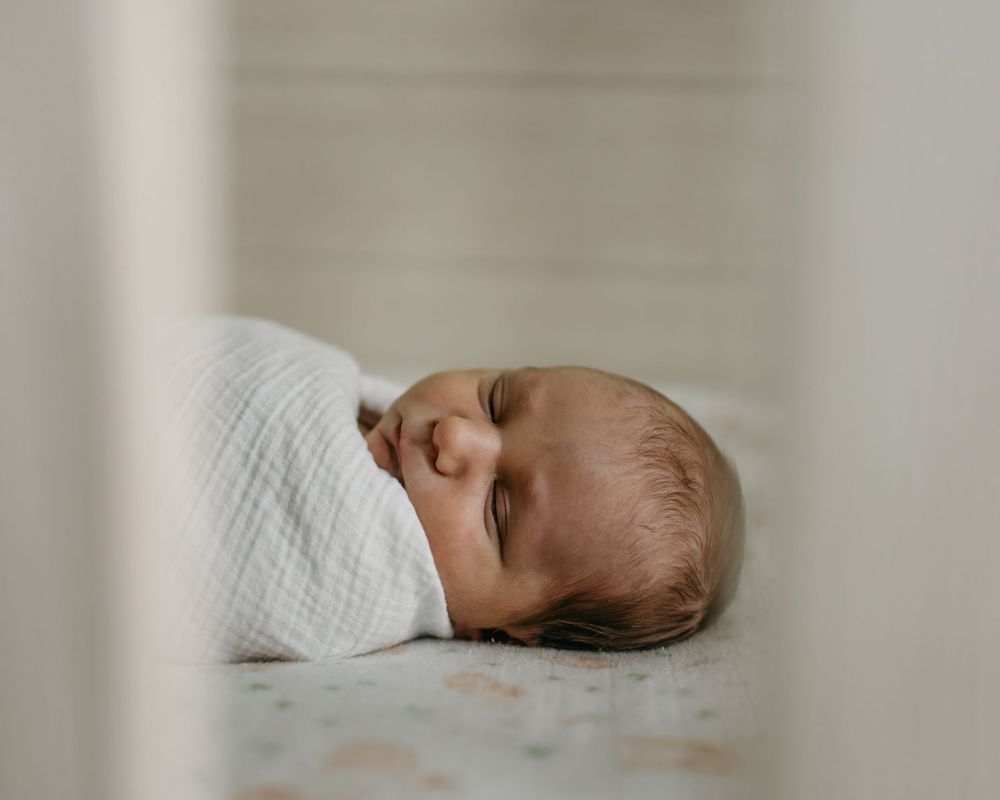 Baby sleeping peacefully on white bedding in soft natural light.