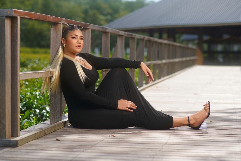 Dancer in black athletic wear stretches gracefully on wooden boardwalk surrounded by greenery.