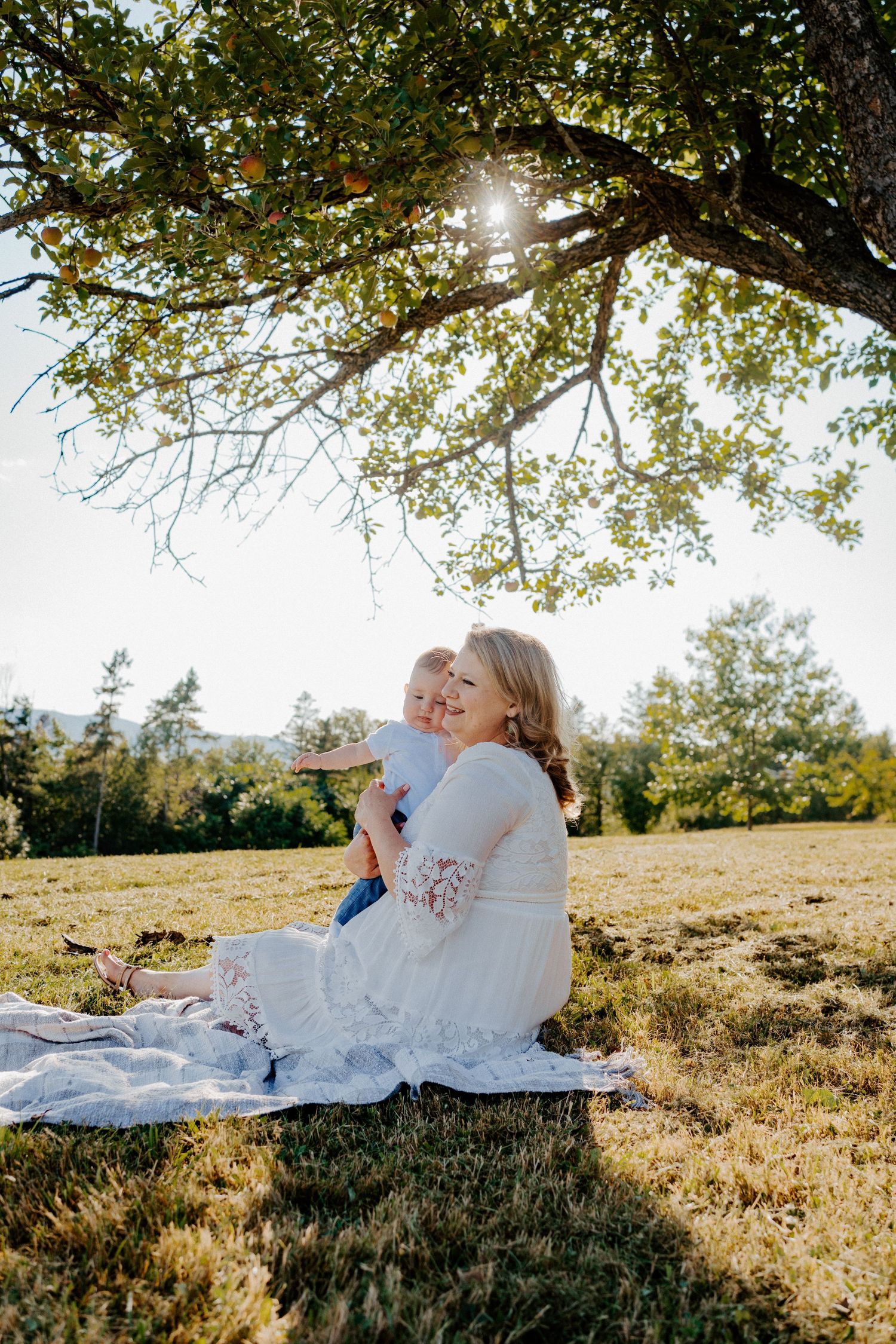 A couple relaxes on a white blanket in a sunlit meadow during a romantic outdoor photoshoot.