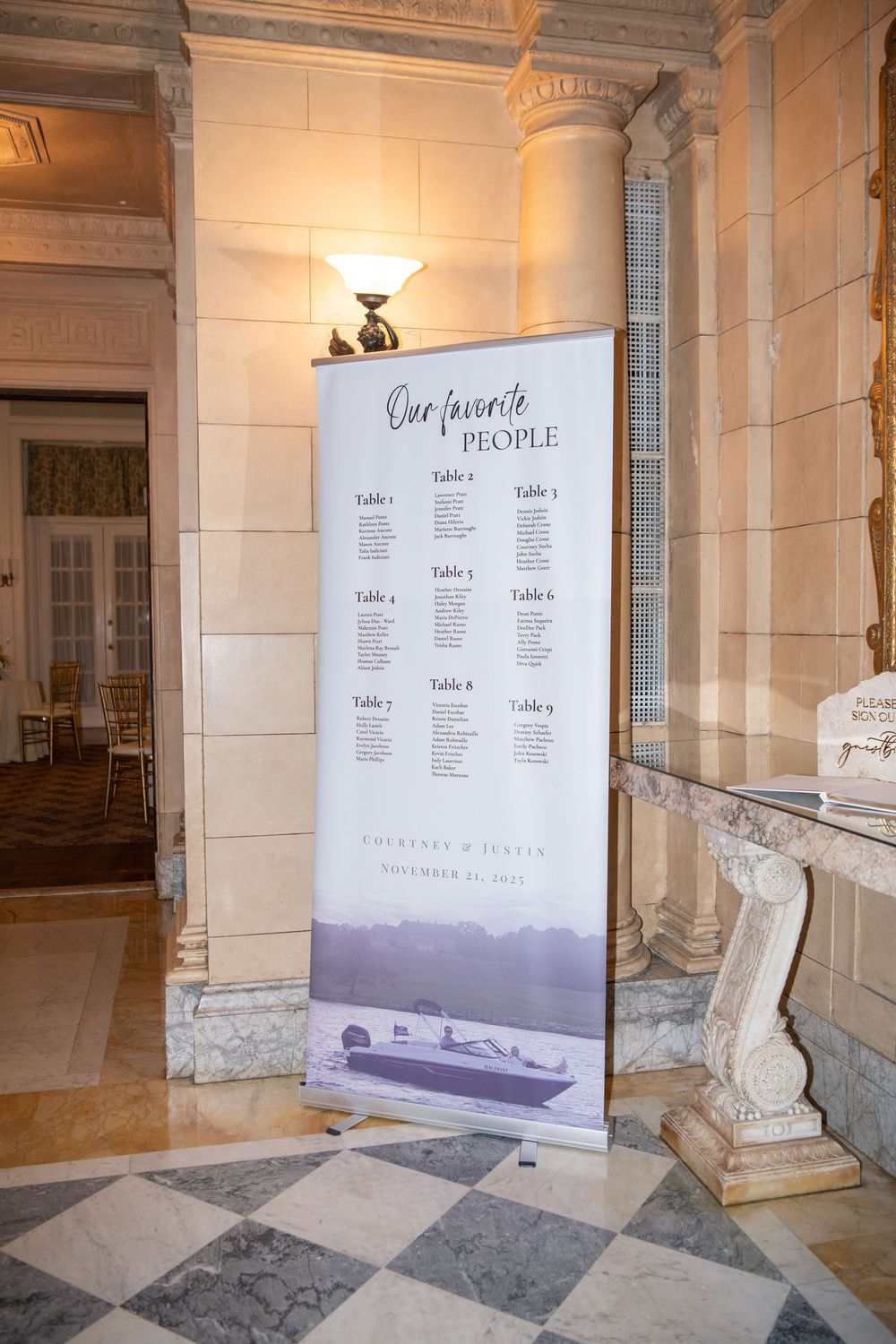 Elegant wedding seating chart display banner in a grand marble hallway with columns.