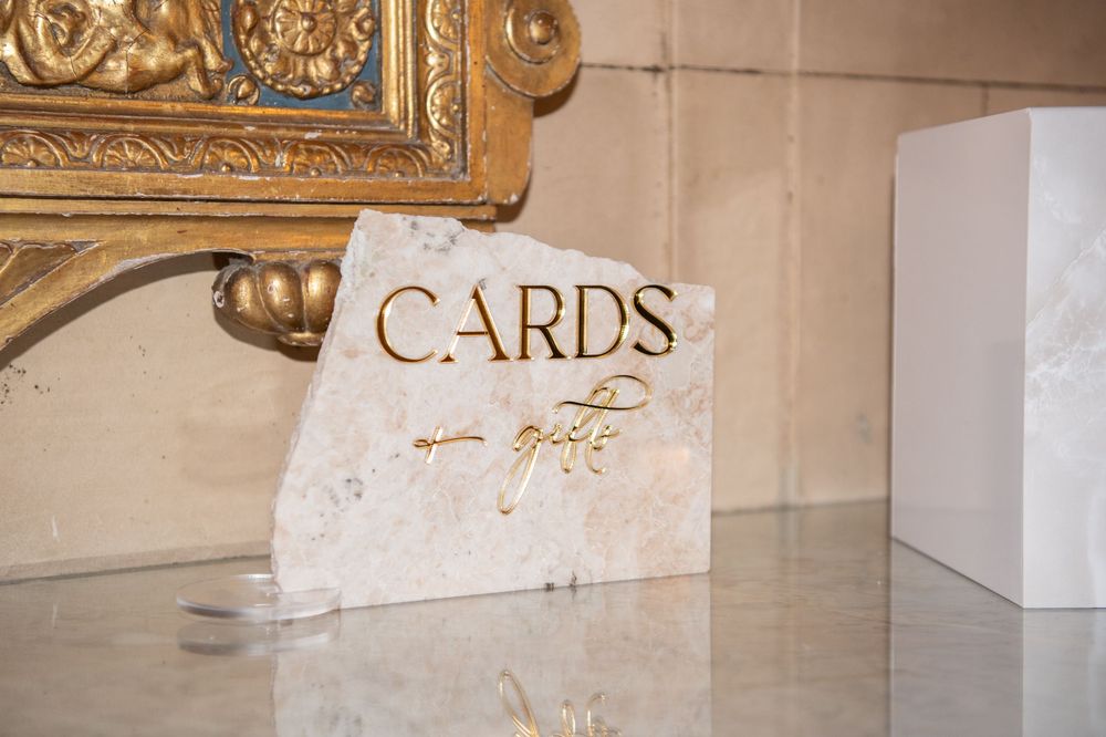Wedding card collection sign displayed on marble surface with ornate gold frame.