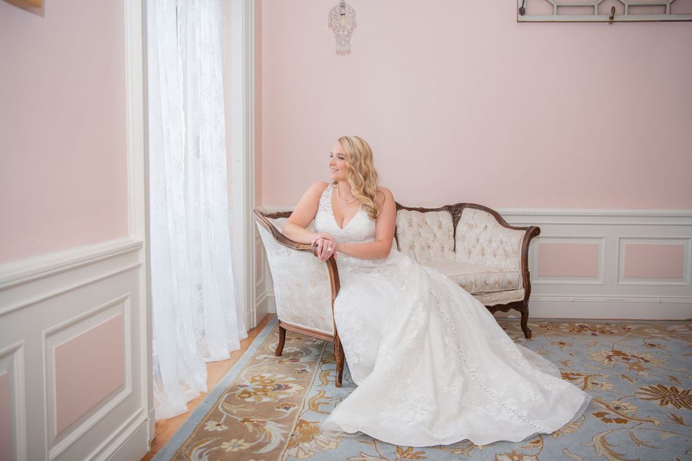 Elegant wedding dress displayed in a pink room with ornate gold mirror and white trim details.