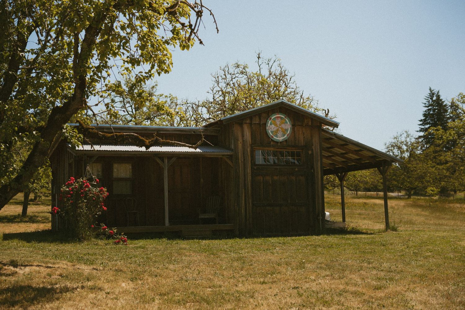 Rustic wooden barn structure with a clock face in a sunny outdoor setting.