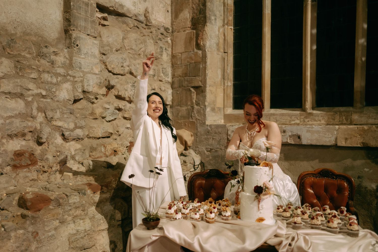 A person in white clothing performs a medieval cooking demonstration in a rustic stone kitchen setting.