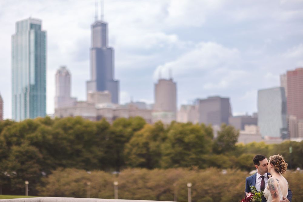 A couple shares an intimate moment against the Chicago skyline with Willis Tower and skyscrapers rising above autumn trees.