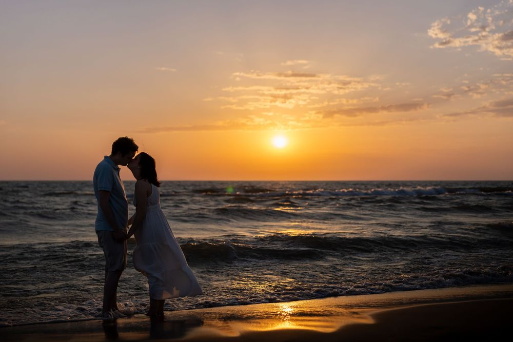 Silhouette of couple embracing on beach during golden sunset over ocean.