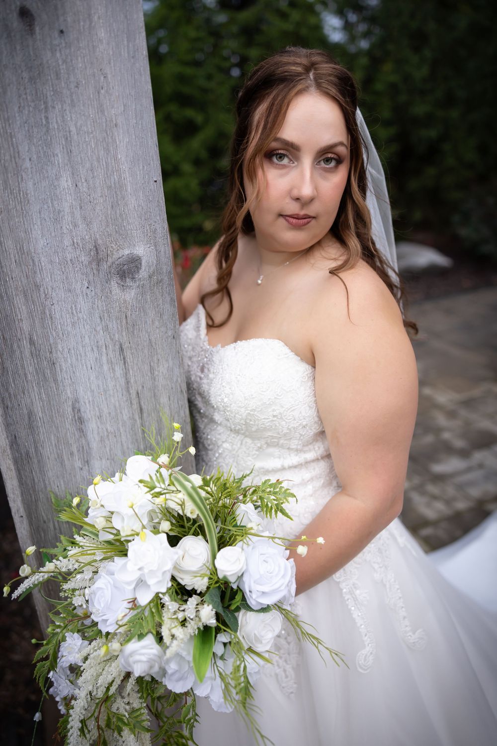 White bridal bouquet with roses and greenery against classic white wedding gown.