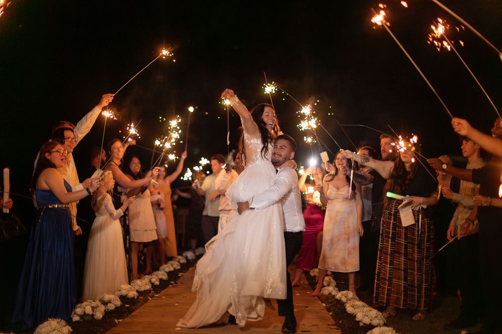 Wedding guests holding sparklers create a magical nighttime tunnel for the celebration.