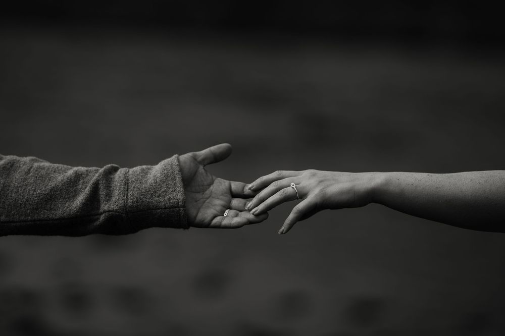 Two hands reaching toward each other in a tender moment, captured in black and white photography.