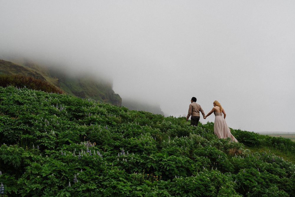 Couple holding hands while hiking through lush green foggy Iceland landscape.
