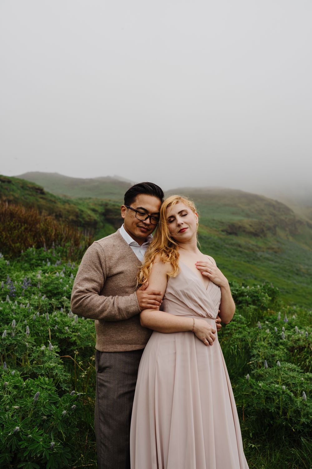 Couple tenderly embracing on green misty hillside, woman in pink gown.