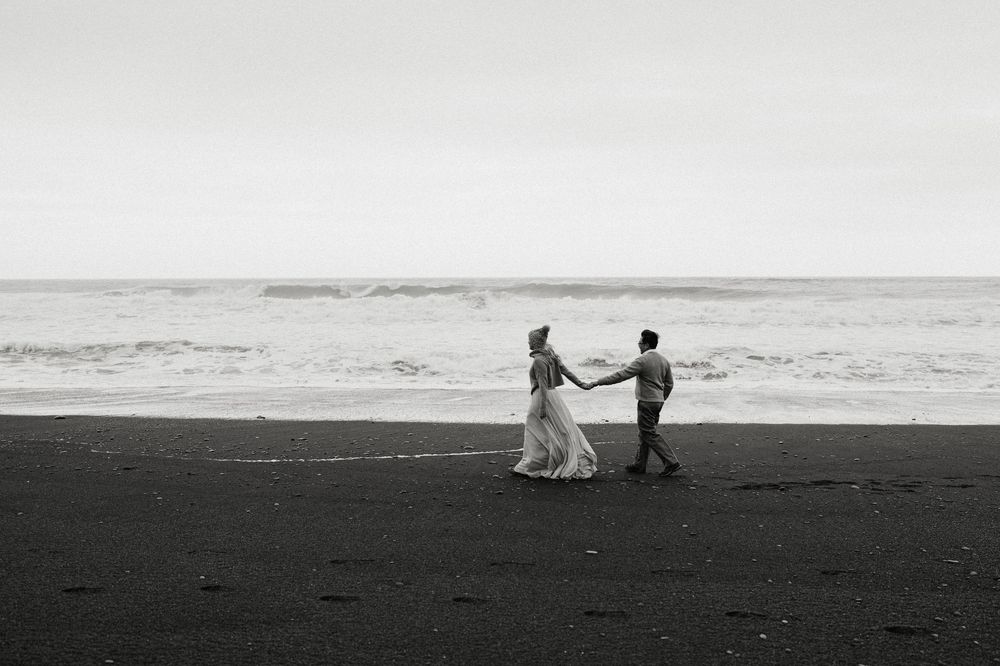 Couple dancing joyfully on black sand beach in black and white photo.