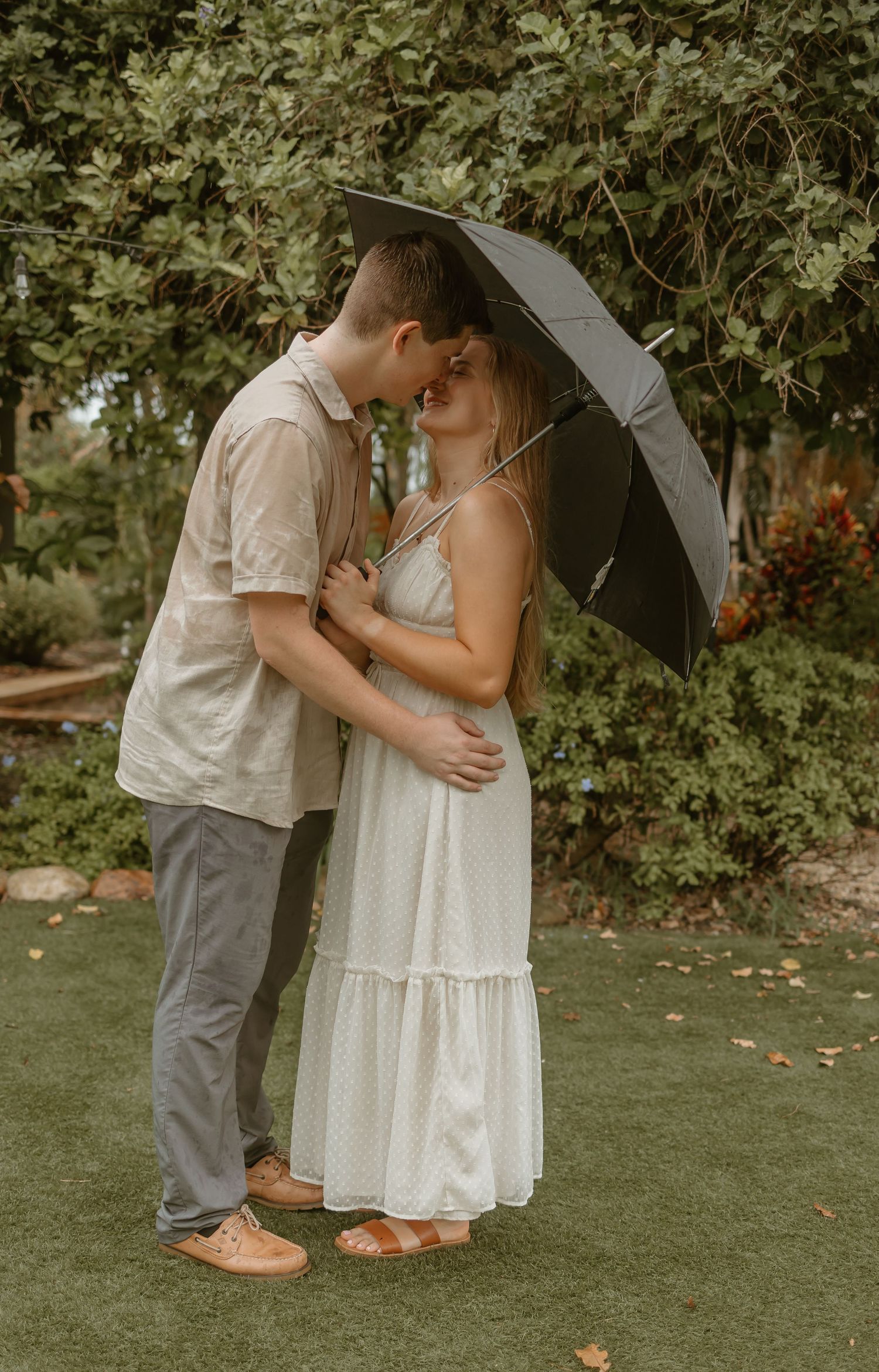 Sweet moment under umbrella in garden setting with white dresses.