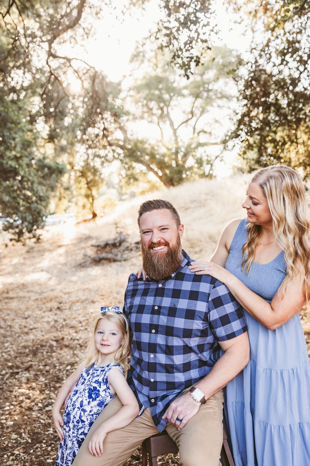Family wearing coordinated blue outfits poses together on a sunny hillside path during golden hour.