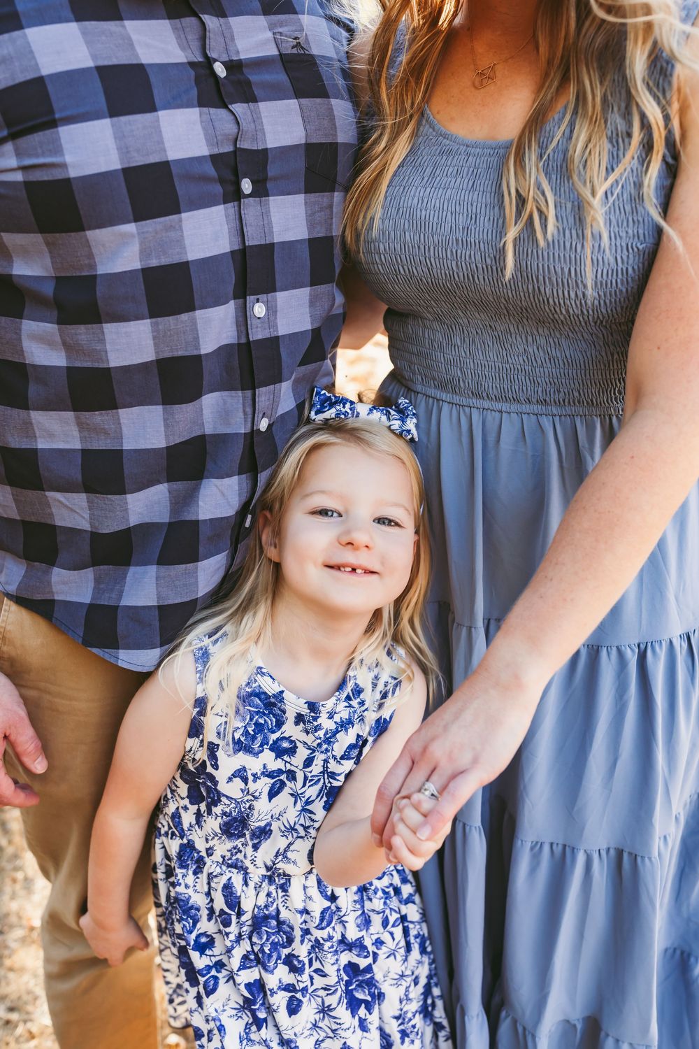 A parent and child in coordinating blue outfits stand together in a series of outdoor family photos.