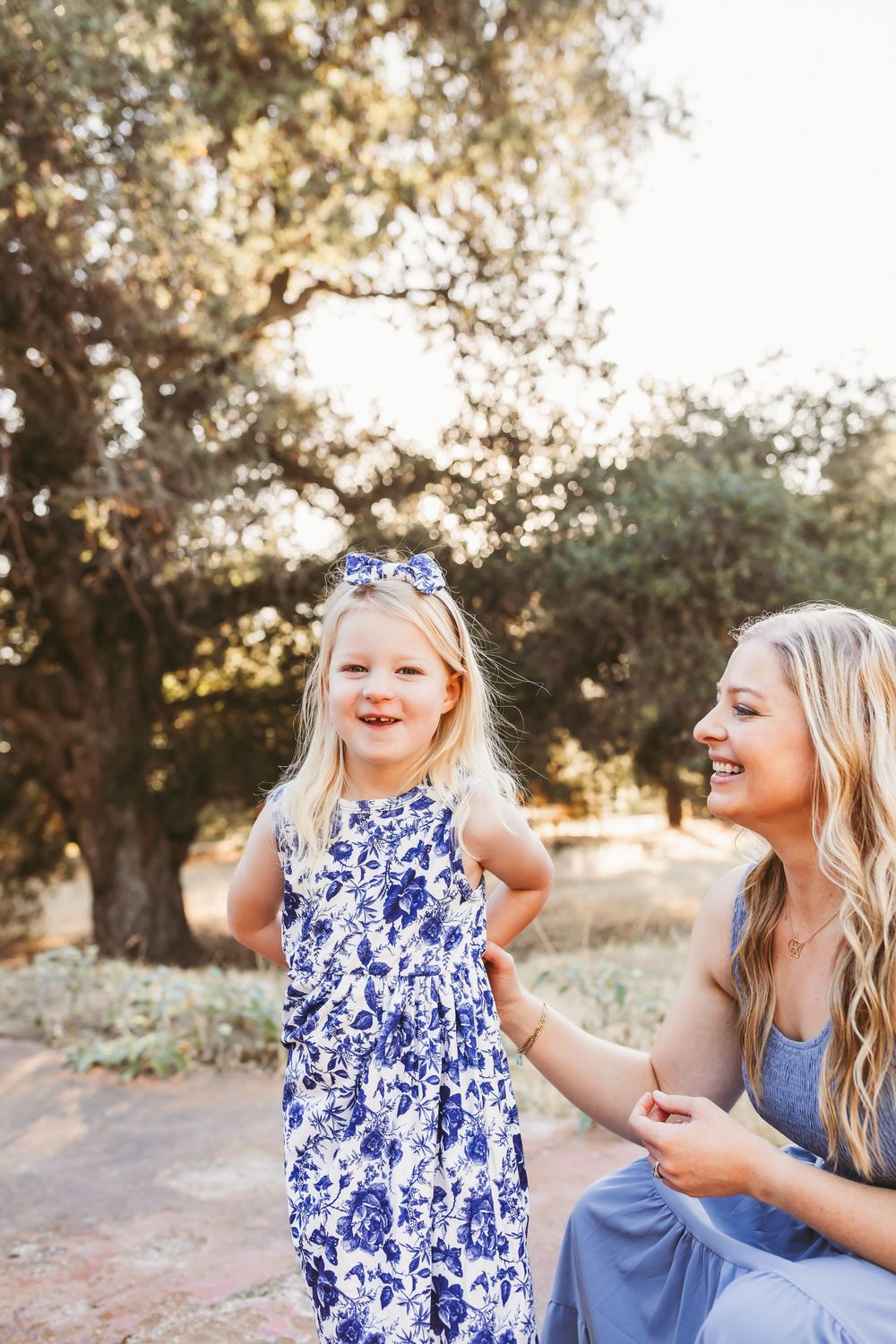 Joyful outdoor photoshoot with blue floral dress and casual attire against a natural sunset backdrop.