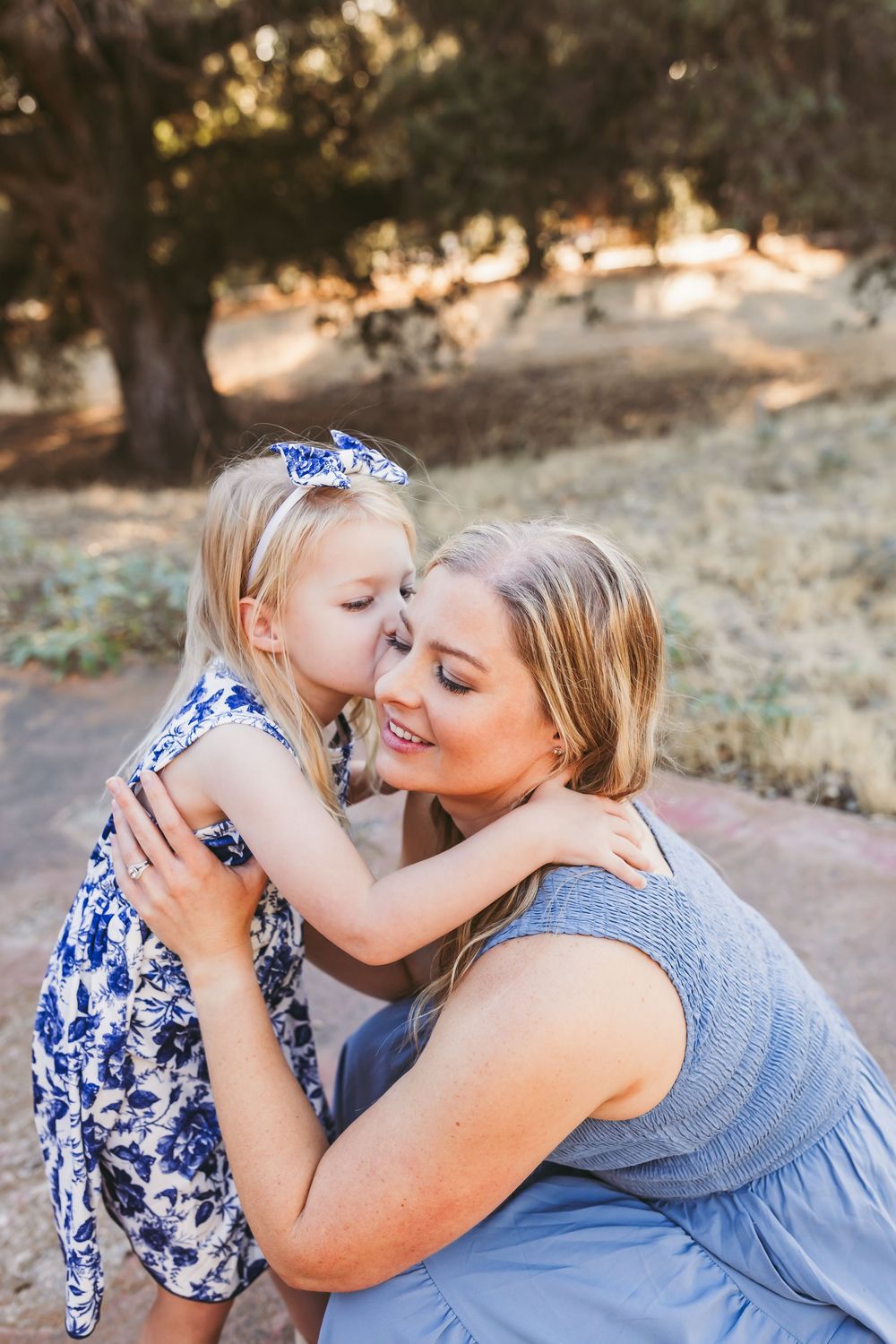 A parent and child wearing blue and white outfits share tender moments together in an outdoor setting during golden hour.