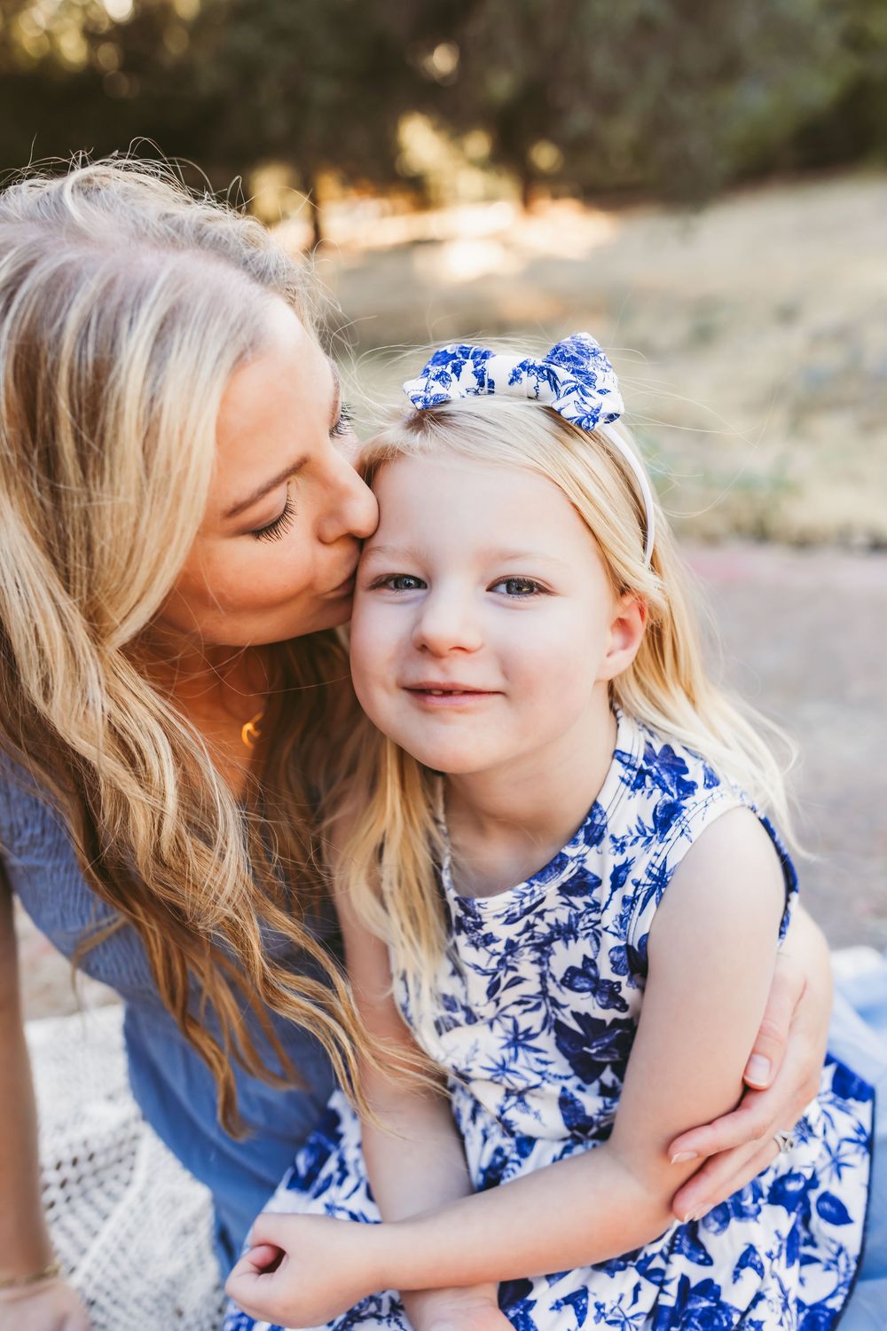 A tender moment between parent and child wearing matching blue and white floral outfits outdoors in natural light.