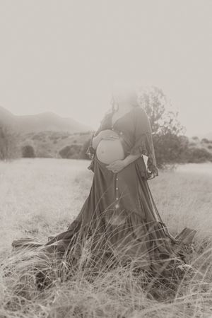 Black and white maternity portrait showing dress movement in natural landscape.
