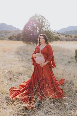 Sunlit maternity session featuring a vibrant red dress in desert terrain.