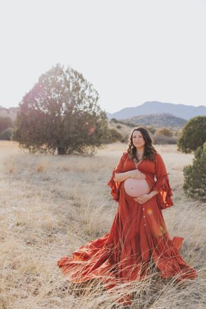Artistic maternity photography with red flowing dress in desert setting.