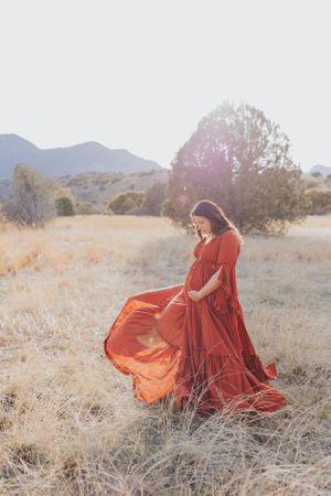 Red dress catches wind during desert maternity photoshoot with mountain backdrop.
