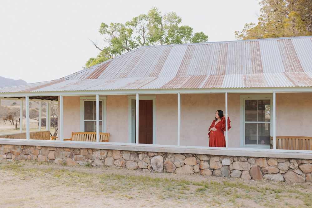 A rustic stone and metal roof building with a wraparound porch in a desert setting.