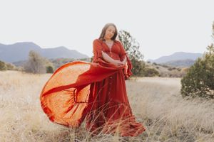 A flowing red dress twirls gracefully against a desert mountain landscape at sunset.