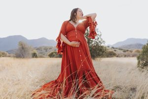 A vibrant red dress flows in the wind against golden grass and mountain backdrop.