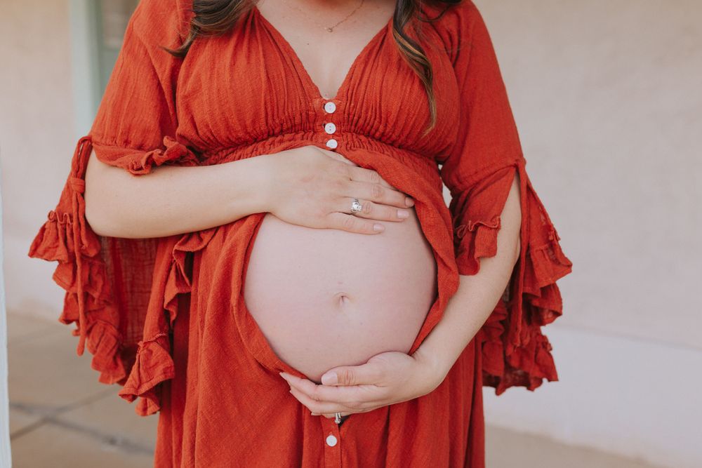Maternity photoshoot in a flowing red dress against a light neutral background.