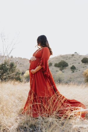 Romantic maternity session featuring a red dress amid dry grass and mountains.