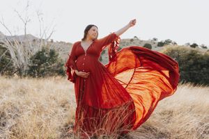 Red dress billows dramatically in the wind during a mountain field photoshoot.