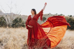 A flowing red dress twirls gracefully in a golden field against a mountain backdrop.