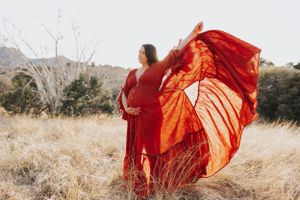 A red dress creates elegant movement against dry grass and mountains.