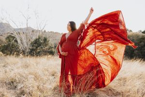 Ethereal red gown flows through the air in a scenic outdoor photoshoot.