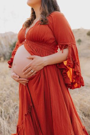 Maternity photo featuring a flowing red empire waist dress in natural outdoor setting.